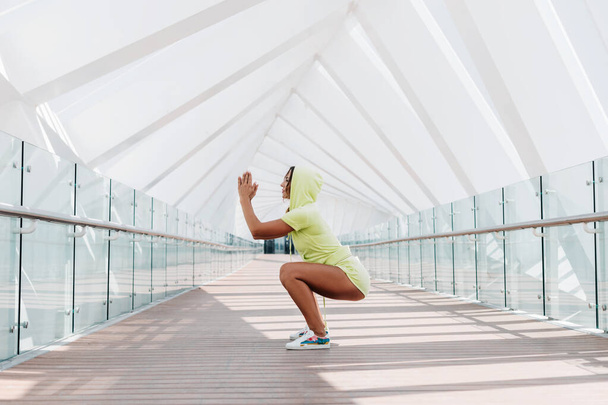Atraktivní žena v teplákové soupravě hraje squats během cvičení. Sport, fitness, zdravý životní styl - Fotografie, Obrázek