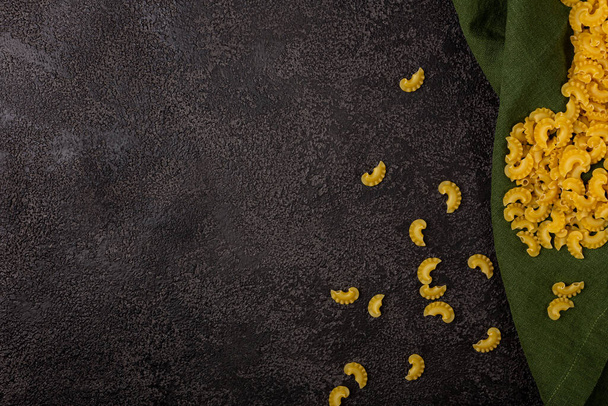 A pile of raw yellow pasta isolated on a dark structural background with space to copy. Pasta top view. Pasta on a green linen napkin - Фото, изображение