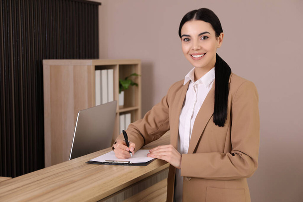 Receptionist with clipboard near countertop in office - Foto, afbeelding