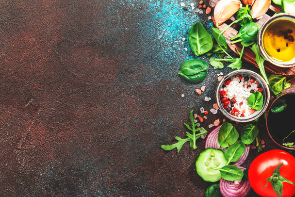 Healthy vegan food background. Ingredients for cooking salad. Cherry tomatoes, spinach, arugula, cucumbers, spices and oil on brown background. Top view - Fotoğraf, Görsel