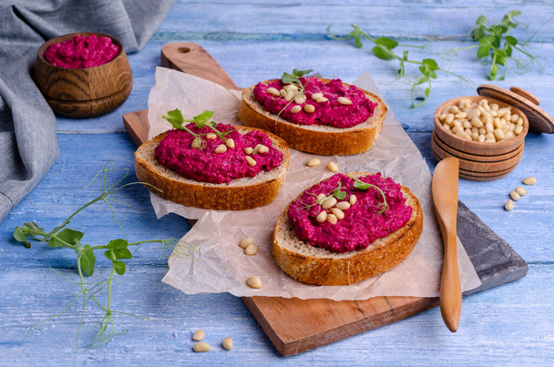 Three sandwiches with beetroot paste, pine nuts and pea sprouts. Blue wooden background. Top view. Selective focus. - Photo, Image
