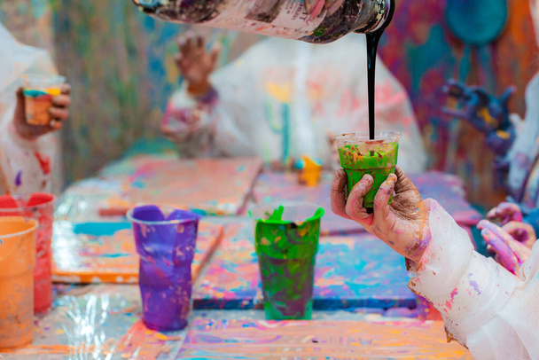 Kleine Kinderhände gießen Acrylfarbe auf eine Leinwand. Abstrakte Maltechnik flüssige Kunst mit flüssigem Acrylglas - Foto, Bild