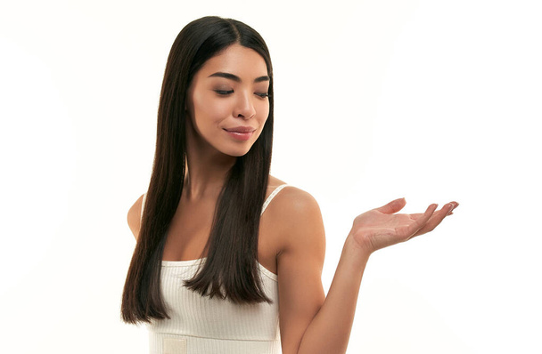 Mladá asijská žena s čistou zářivou zdravou pletí drží na dlani, ukazuje na výrobku izolované na bílém pozadí. Péče o pleť, kosmetologie, lázně. - Fotografie, Obrázek
