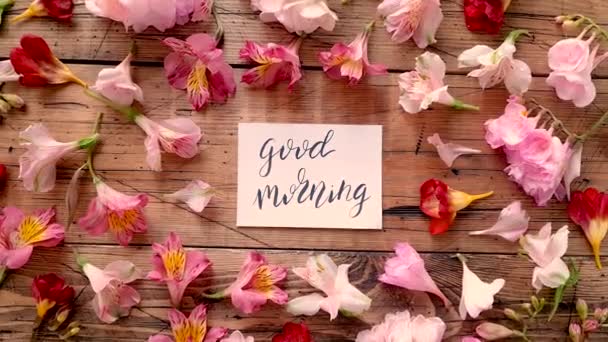 Bom dia cartão perto de flores em uma mesa de madeira vista superior  - Filmagem, Vídeo