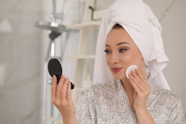 Beautiful young woman applying face powder with puff applicator in bathroom at home - Fotografie, Obrázek