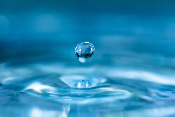 ガラスの青い色の水に水滴が飛び散って水を反射しています. - 写真・画像