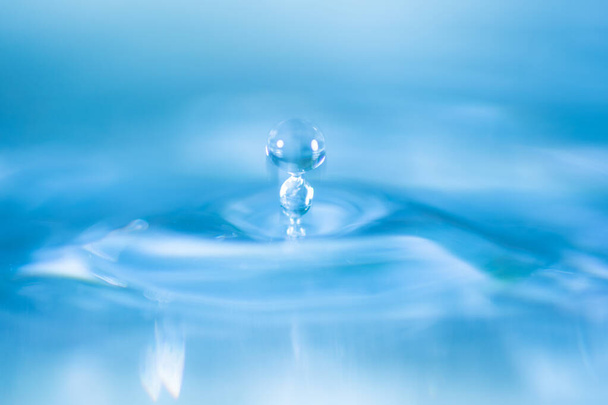 goccia d'acqua spruzzare in un bicchiere blu colpo colorato di acqua che gocciola e riflette l'acqua. - Foto, immagini