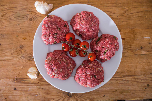 Raw hamburgers on a plate with tomatoes and garlic. - Fotó, kép