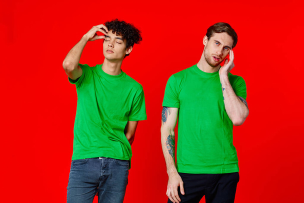 Két zöld pólós barát áll a bádogdoboz mellett, kezükkel érzelmekkel, vörös háttér. - Fotó, kép