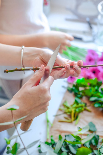 Les mains de la personne coupant avec le couteau les fleurs vertes et roses - Photo, image