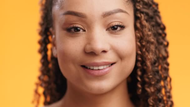 Πορτρέτο του χαριτωμένο νεαρή μαύρη κυρία με afro hairstyle χαμογελώντας στην κάμερα, πορτοκαλί φόντο στούντιο, αργή κίνηση - Πλάνα, βίντεο
