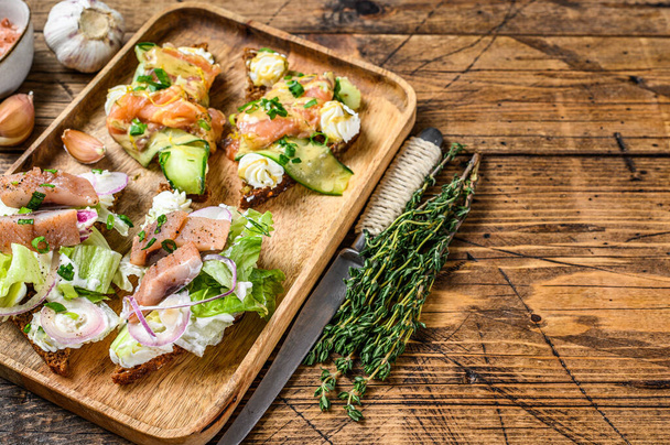 Open sandwich with salmon and herring, cream cheese and salad on a cutting board. wooden background. Top view. Copy space - Фото, зображення