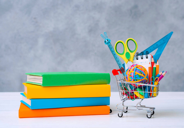 Colorful school supplies in the shopping basket on a gray background with a copy of the text space. A stack of books with colorful covers. - Photo, Image