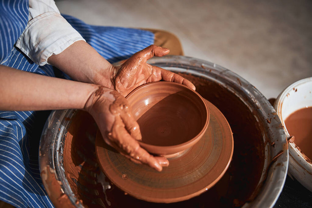 Female hands shaping clay pot on special wheel - Foto, afbeelding