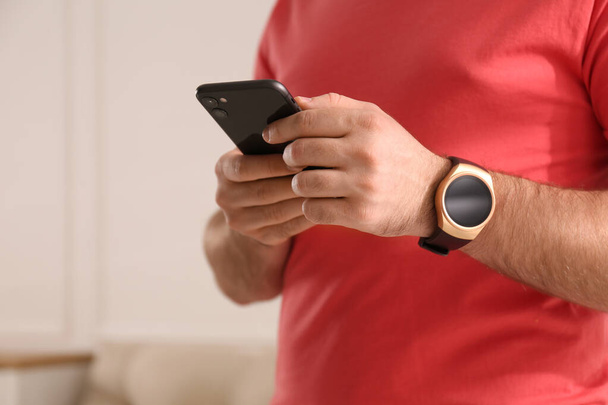 Young man with smart watch and phone at home, closeup. Space for text - Foto, Imagem