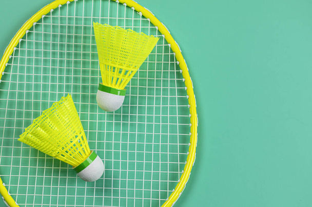 Yellow and red badminton rackets with shuttlecocks on bright green background top view flat lay. - Photo, image
