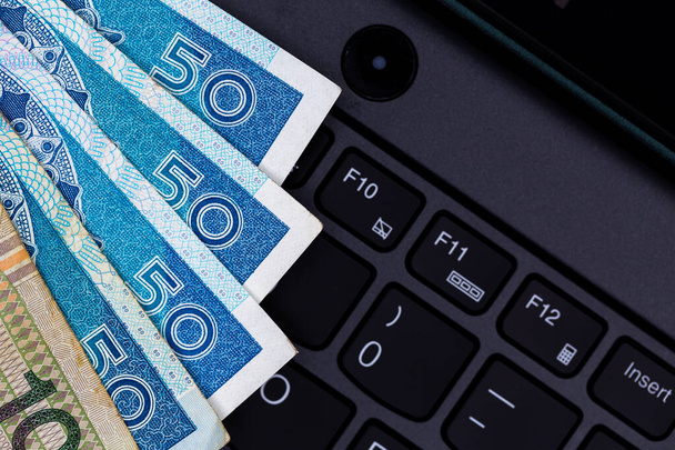A set of Polish 50 and 100 PLN banknotes arranged on a black laptop keyboard. Photo taken under artificial, soft light - Fotó, kép