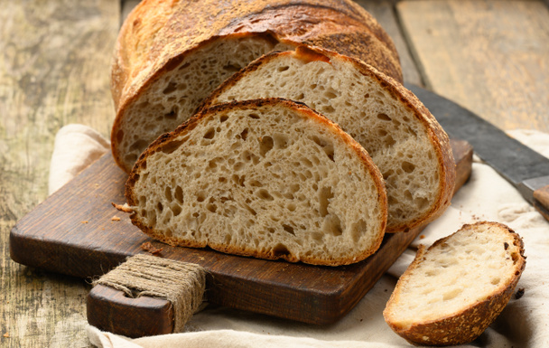 выпечка круглого хлеба из белой пшеничной доски на деревянной доске, хлеб нарезанный на куски, крупным планом - Фото, изображение