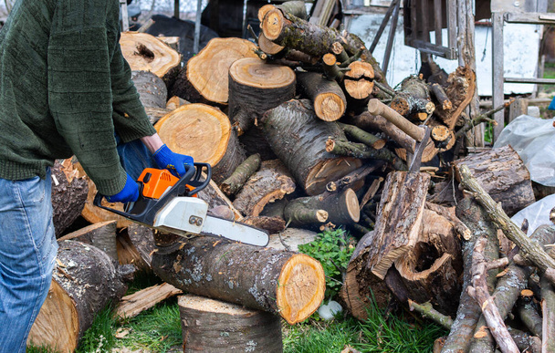 Preparando legna da ardere per l'inverno, tronchi di ciliegio accatastati in un mucchio nel cortile, un agricoltore segare un tronco con una motosega - Foto, immagini