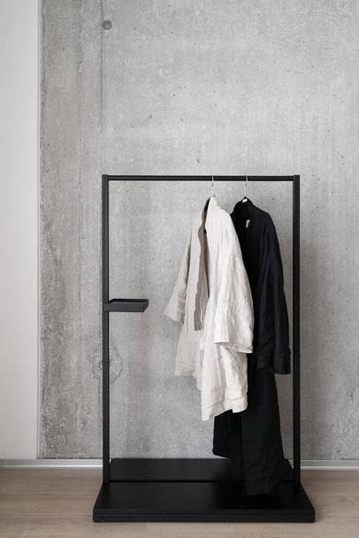 Colpo verticale di kimono casual in bianco e nero a tutta lunghezza appeso su appendiabiti in metallo nero contro muro di cemento grigio. Showroom e shopping concept - Foto, immagini