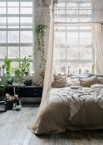 Crop shot bohém stílusú hálószoba, kényelmes, de king size hangulatos ágy sok párnák és baldachin, fekete antik fiók növényekkel körülvéve, nagy fehér széles ablakok cserepes növényzet - Fotó, kép