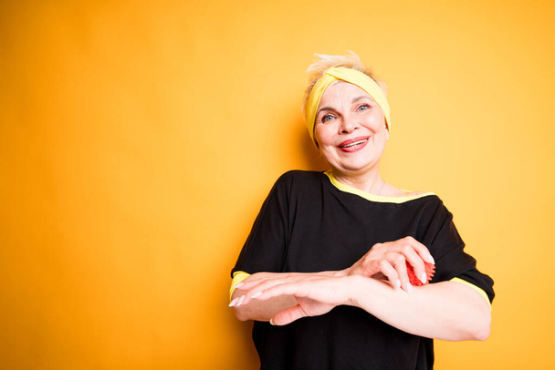 Beautiful elderly woman doing exercises on the muscles of the arms using a massage ball. Isolated on yellow background - Fotografie, Obrázek