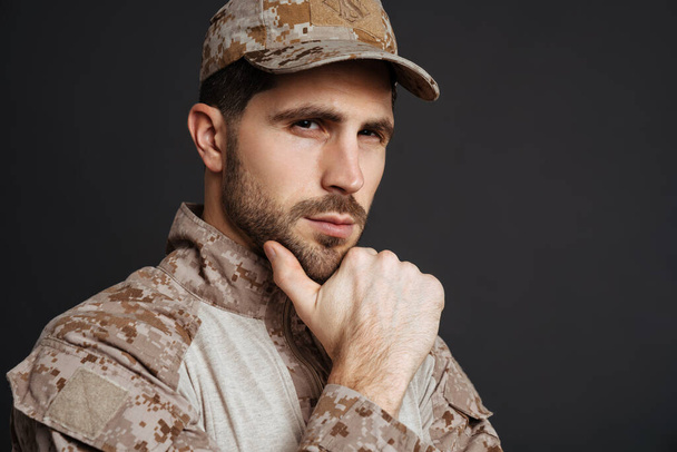Thinking masculine military man posing and looking at camera isolated over black background - Фото, зображення