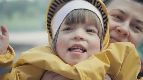 Moeder pikt een kind op in een geel jasje met een kap in haar armen. close-up schot - Video