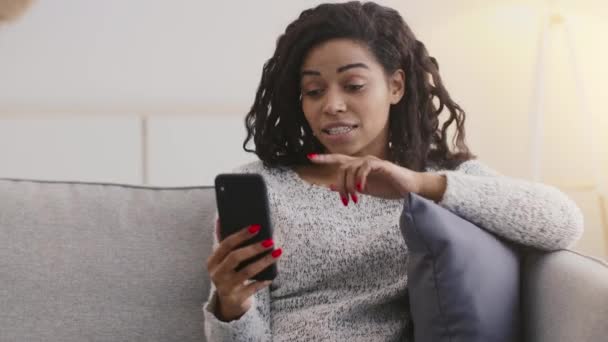 Joven afroamericana dama videollamadas a amigos, hablando a través de la aplicación de teléfono inteligente, sintiéndose sorprendido por las noticias en casa - Metraje, vídeo