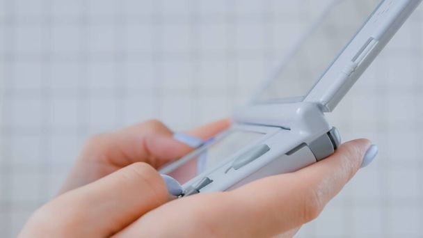 Close up side view of woman using grey portable game console against tile wall - Photo, Image