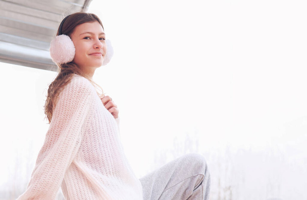 happy teenager girl sitting on a reels and smiling looking at camera. girl wearing ear muffs and enjoying outdoor leisure. copy space. - Foto, Imagem