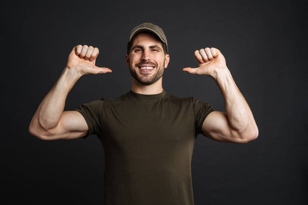 Happy military man celebrating success isolated over black wall, pointing fingers at himself - Photo, Image