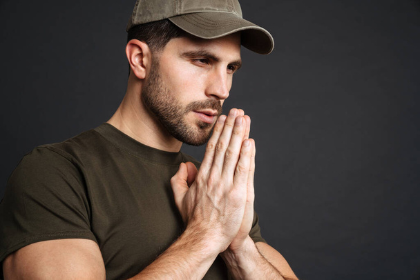 Focused masculine military man making praying gesture isolated over black background - Foto, Imagen