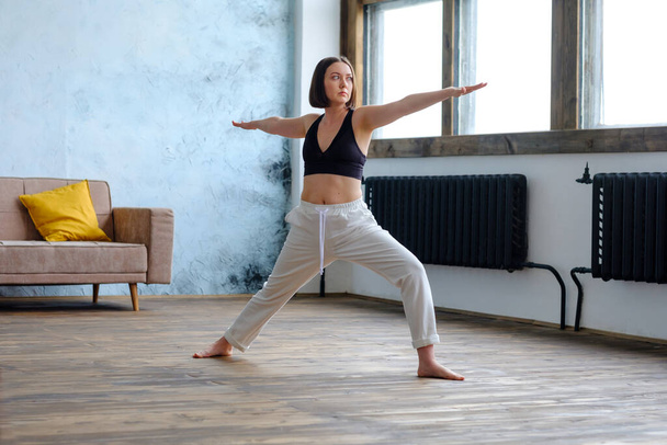 Woman in her living room in warrior yoga pose. - Foto, afbeelding