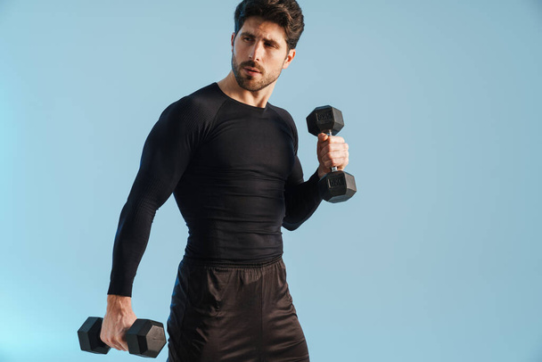 Handsome athletic sportsman working out with dumbbells isolated over blue background - Fotoğraf, Görsel
