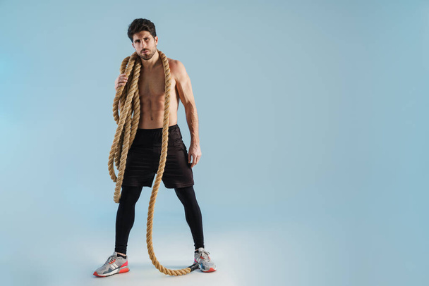 Shirtless athletic sportsman posing with battle ropes isolated over blue background - Fotografie, Obrázek