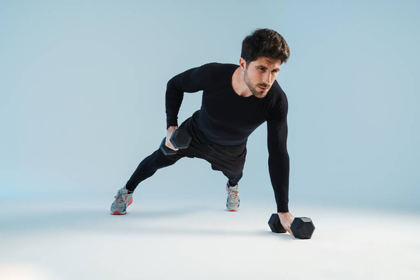 Handsome athletic sportsman working out with dumbbells isolated over blue background - Fotó, kép