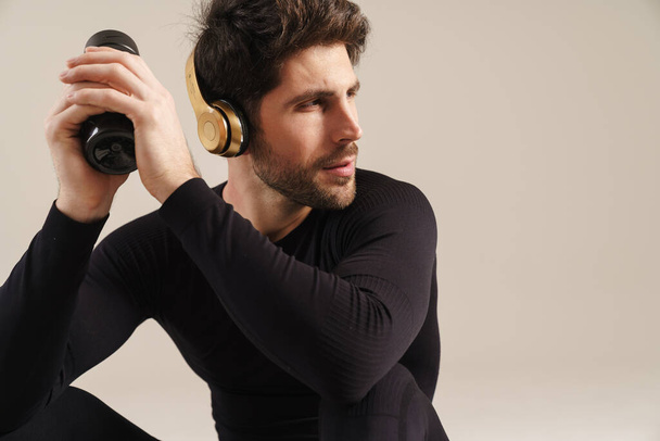 Focused athletic sportsman in headphones looking aside isolated over grey background - Fotó, kép