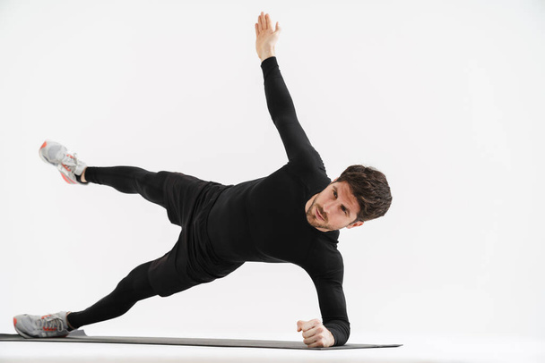 Young athletic sportsman doing exercise while working out on mat isolated over white background - Fotó, kép