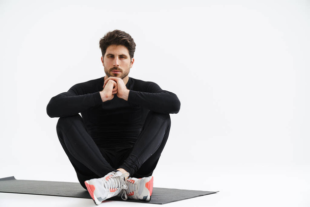 Young athletic sportsman sitting on mat during workout isolated over white background - Valokuva, kuva