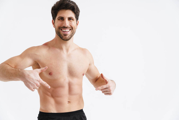 Shirtless joyful sportsman pointing fingers at his abs isolated over white background - Zdjęcie, obraz