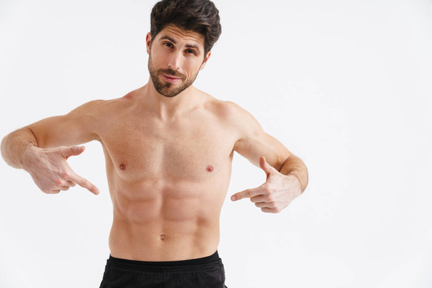 Shirtless pleased sportsman pointing fingers at his abs isolated over white background - Foto, Imagem