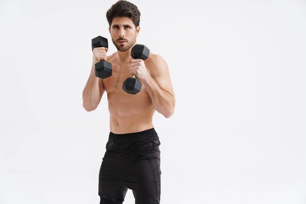 Half-naked athletic sportsman working out with dumbbells isolated over blue background - Fotografie, Obrázek