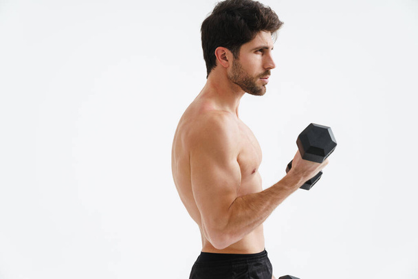Half-naked athletic sportsman working out with dumbbell isolated over blue background - Foto, afbeelding