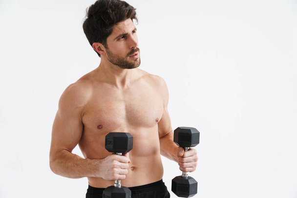 Half-naked athletic sportsman working out with dumbbells isolated over blue background - Foto, immagini