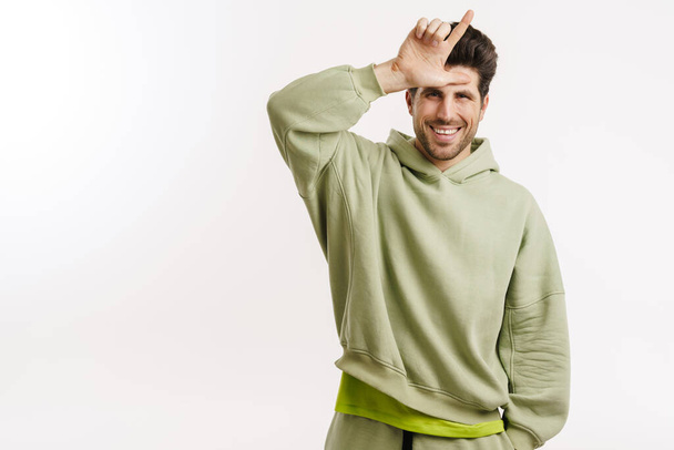 Happy handsome man in sportswear smiling and pointing finger upward isolated over white background - Foto, afbeelding