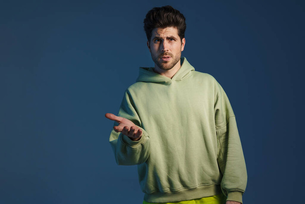 Perplexed handsome man in sportswear posing and gesturing at camera isolated over blue background - Zdjęcie, obraz