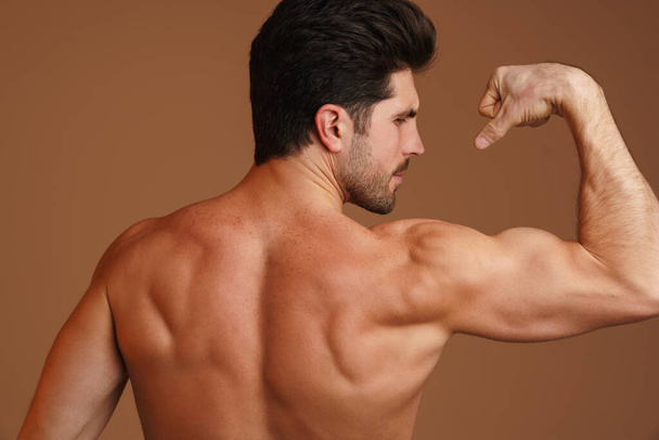Shirtless athletic man showing his biceps at camera isolated over beige background - Foto, Imagem