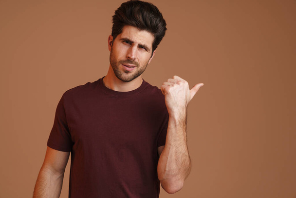 Confused masculine man posing and pointing finger aside isolated over beige background - Fotoğraf, Görsel