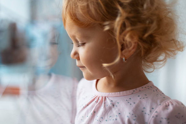 Side portrait of thoughtful child girl near window. Reflection of face on glass. - Photo, Image